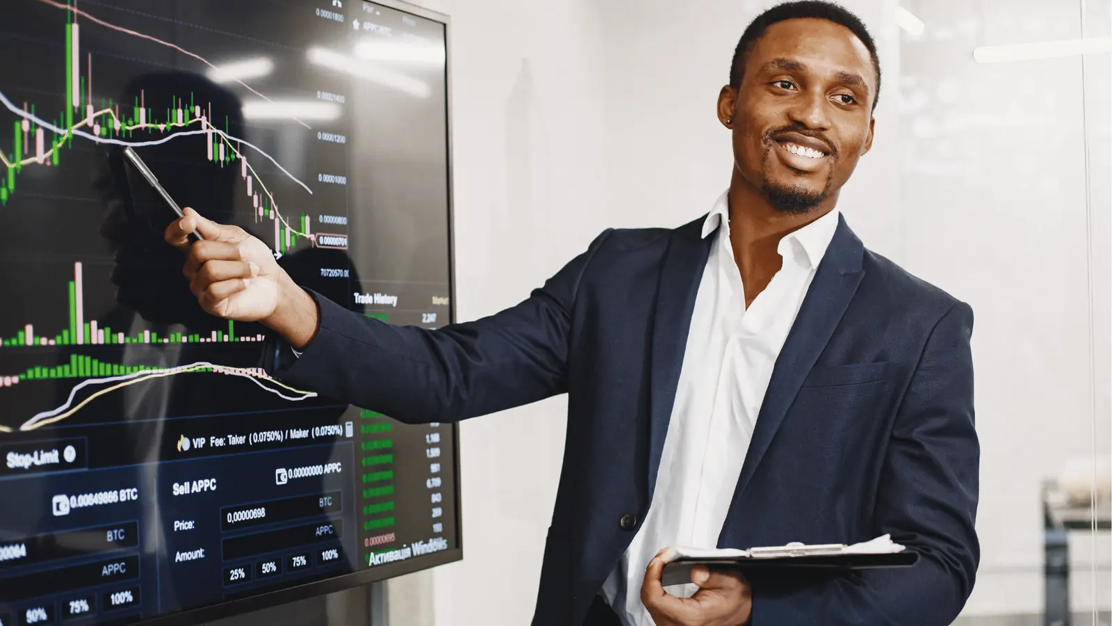 Smiling businessman pointing at large trading chart on screen holding a tablet for AI-assisted workflow