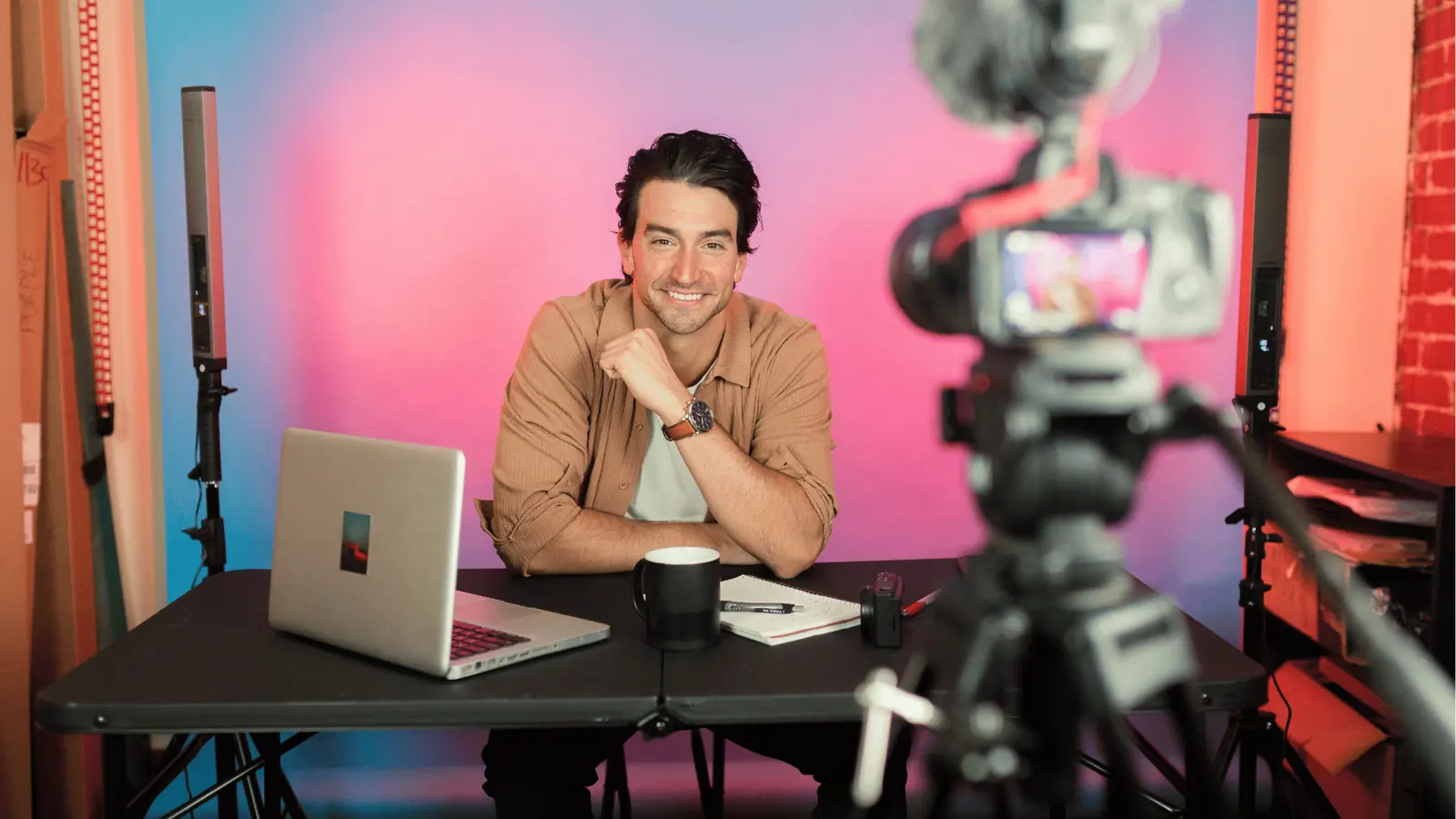 Smiling content creator sits at desk recording a video with camera for workflow