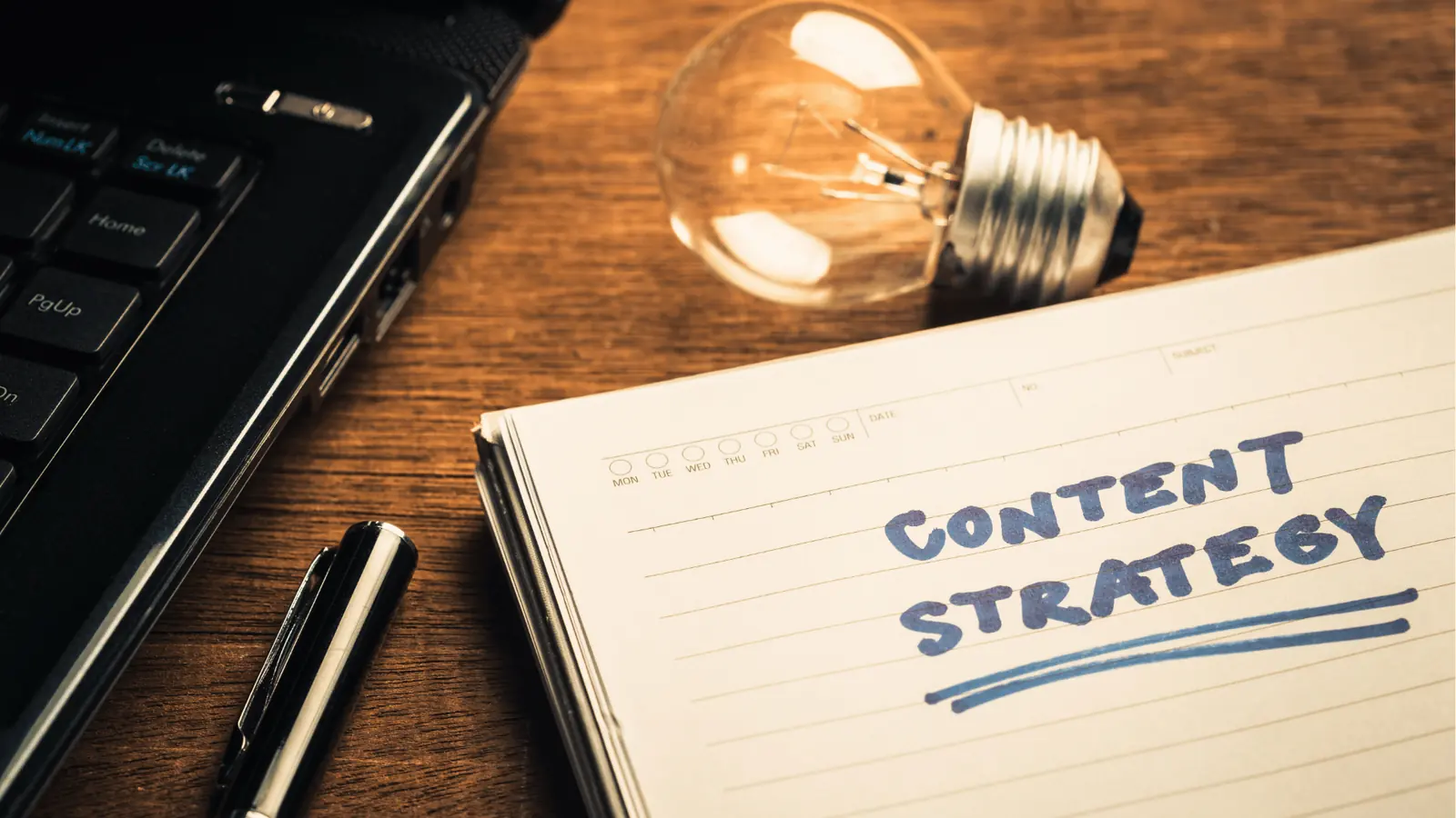 Notebook on wooden desk with handwritten 'Content Strategy' beside laptop for multi-brand management