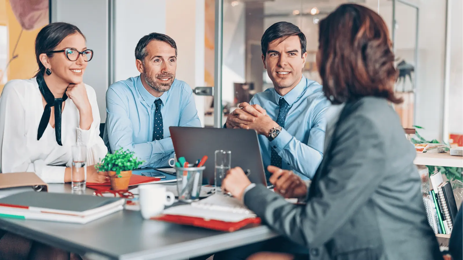 Four colleagues in a bright office meeting around a laptop and documents for content calendar