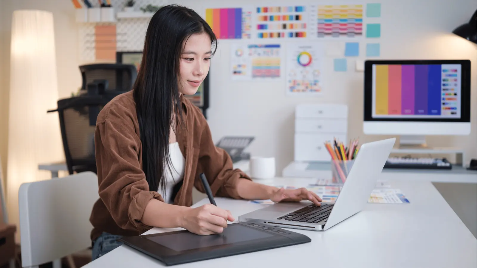 Woman using graphics tablet and laptop at a color-design workspace for publishing