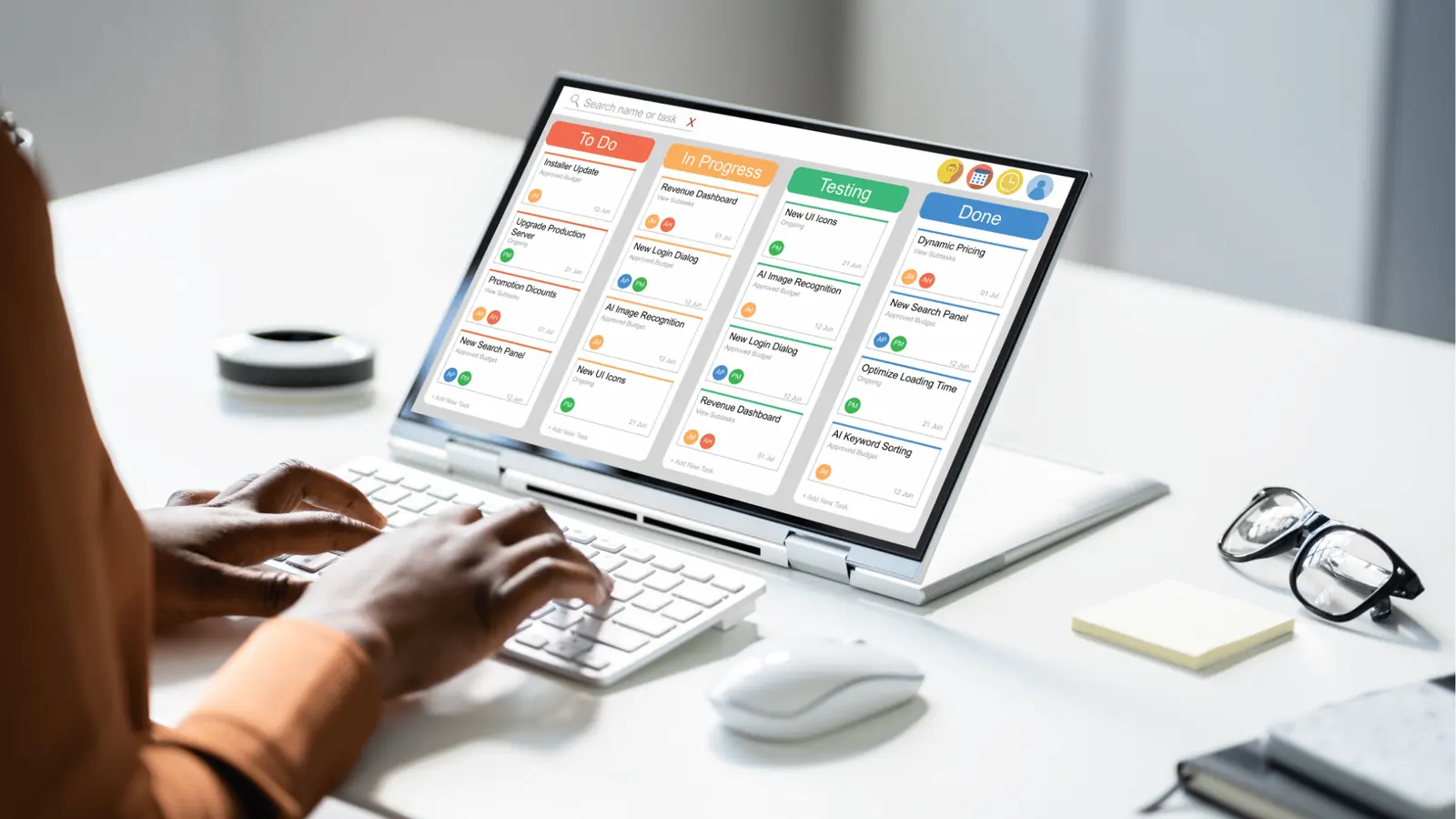 Hands typing by laptop showing a kanban task board with colored columns for approval workflow