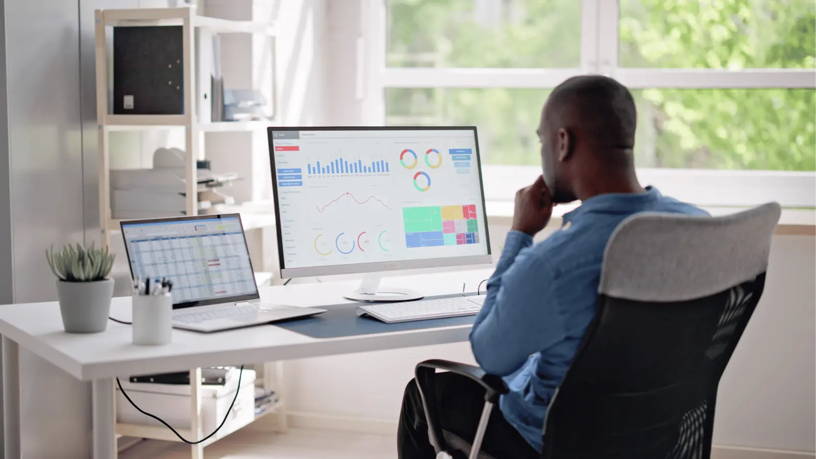 Man sitting at desk looking at analytics dashboards on dual monitors for brand management