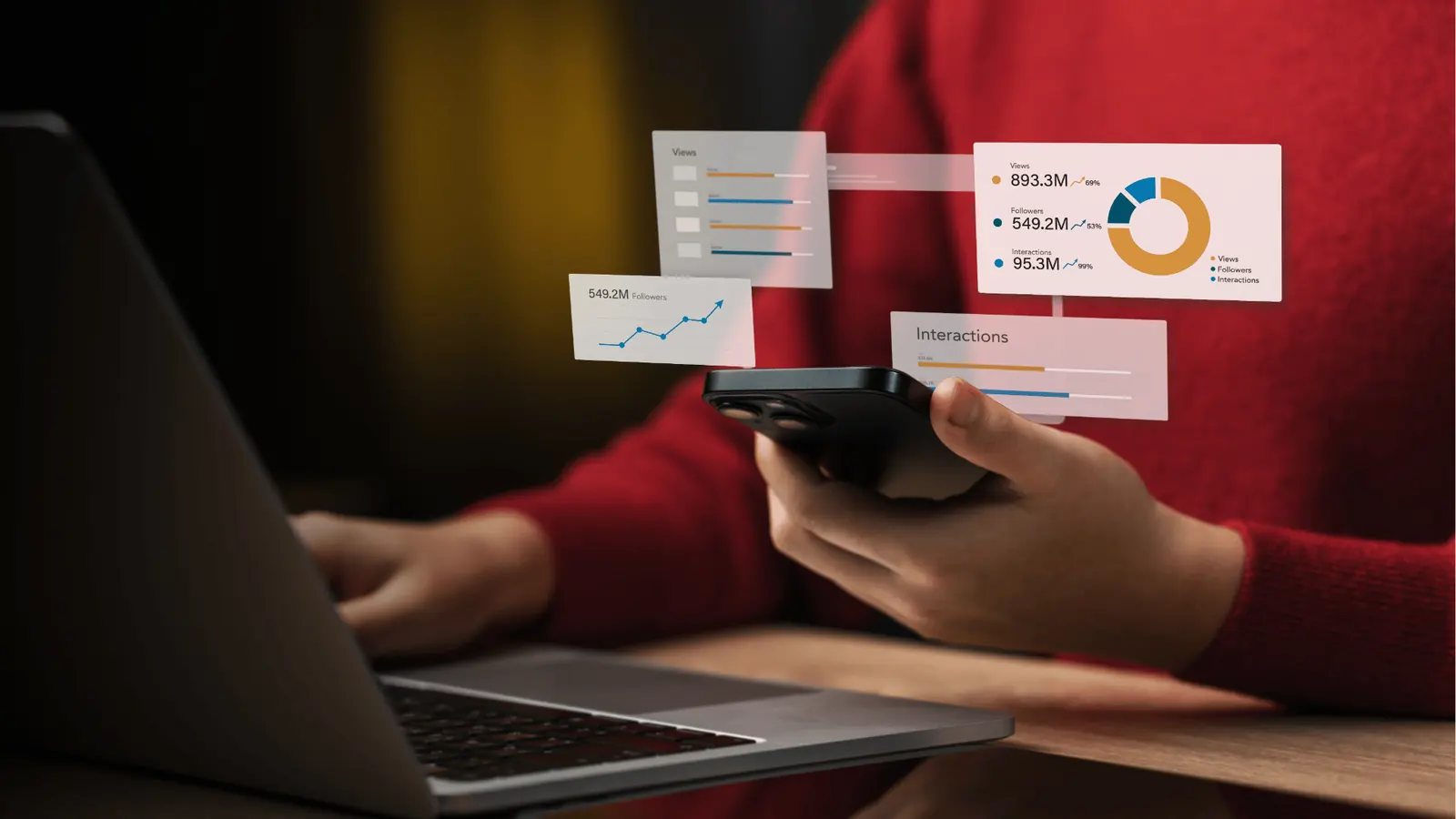 Person holding smartphone beside laptop with floating analytics charts for workflow
