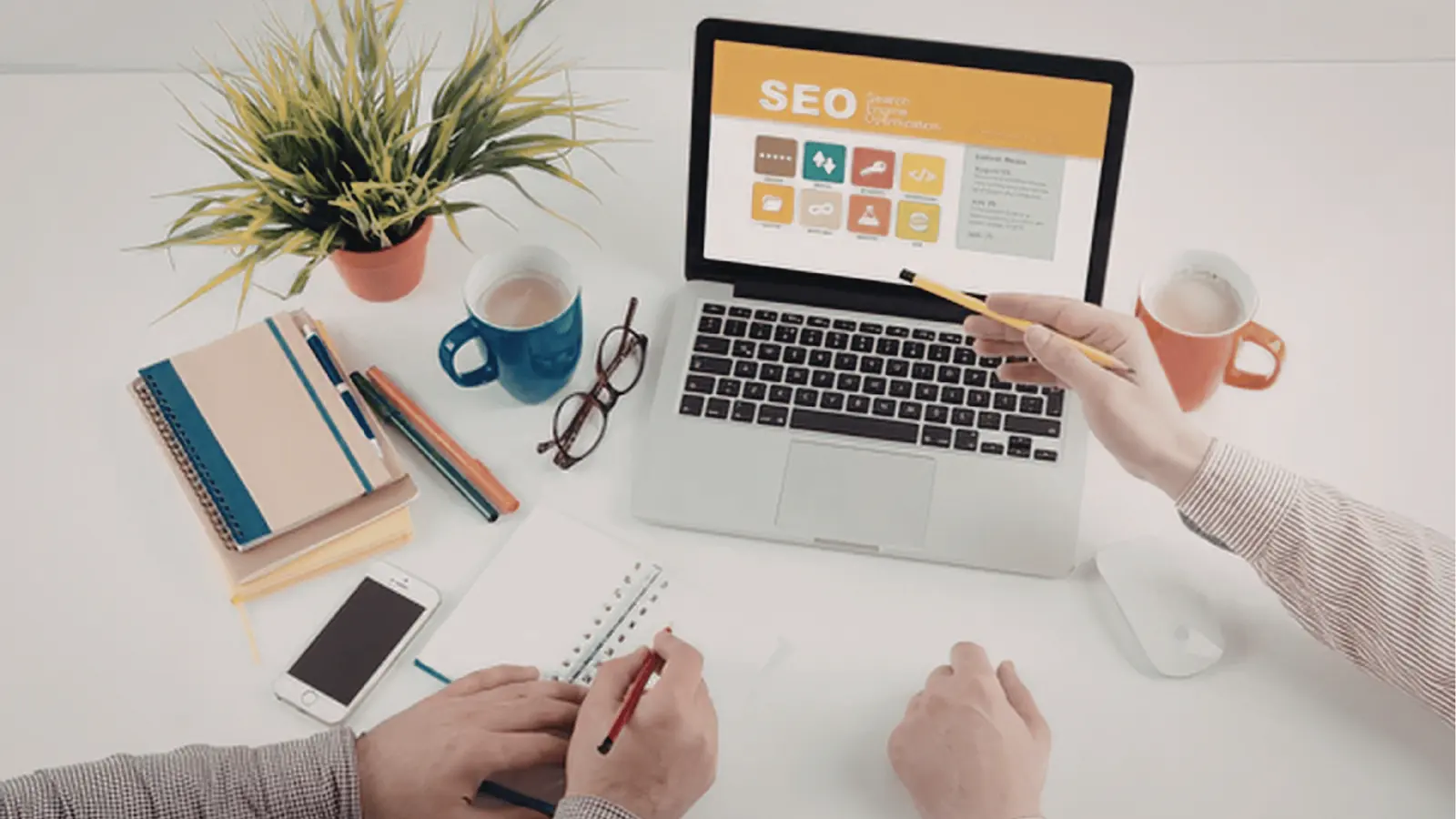 Overhead view of two people working at desk with laptop showing SEO screen for multi-brand management