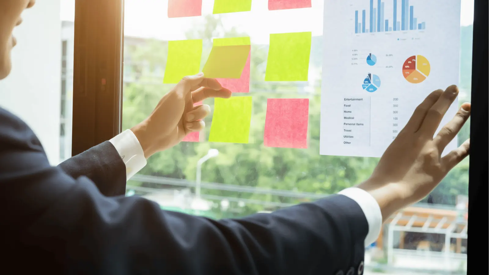 Person placing pink and yellow sticky notes on window next to printed chart for analytics