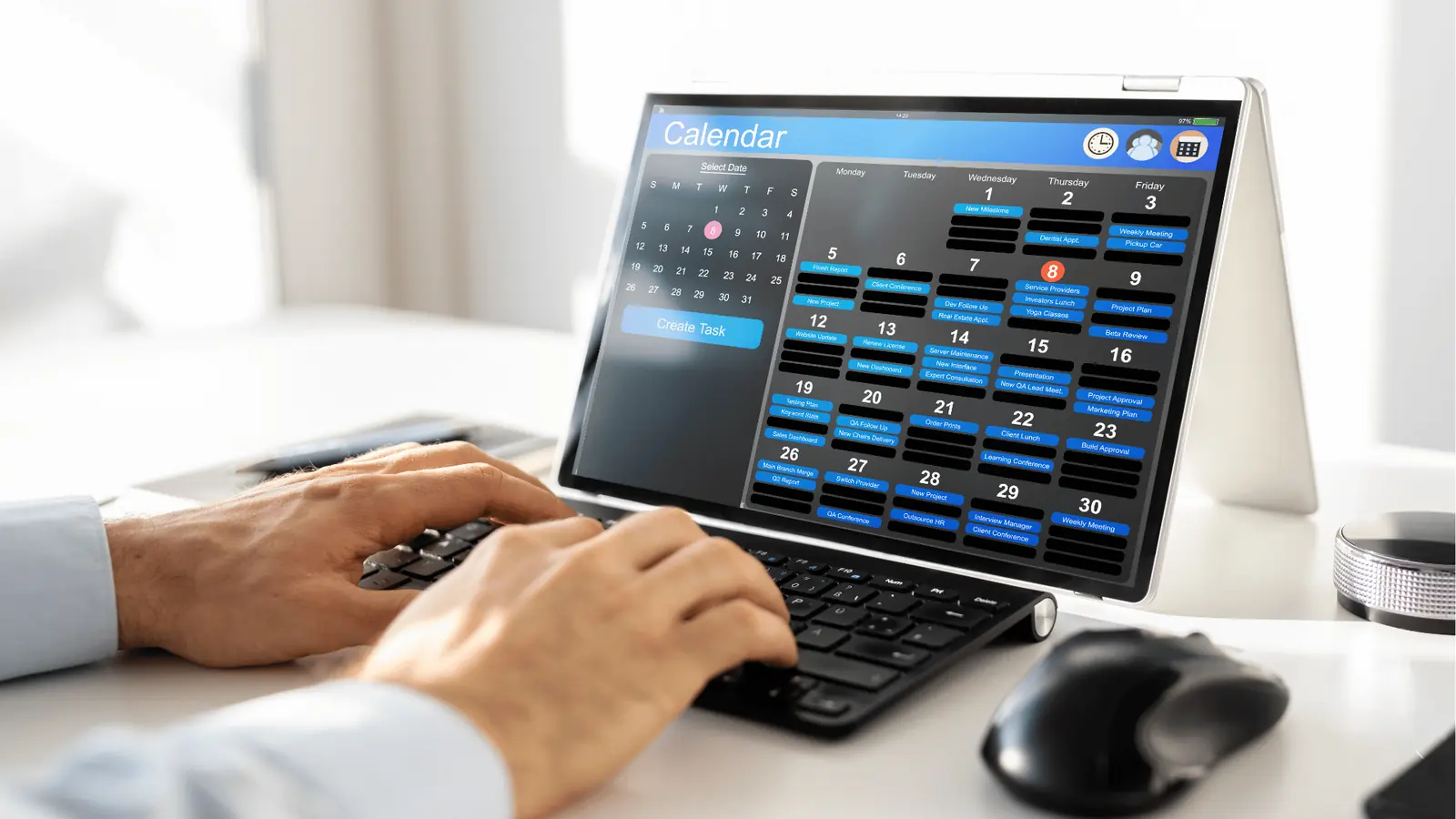 Person typing on keyboard next to tablet showing a monthly calendar app for creative production