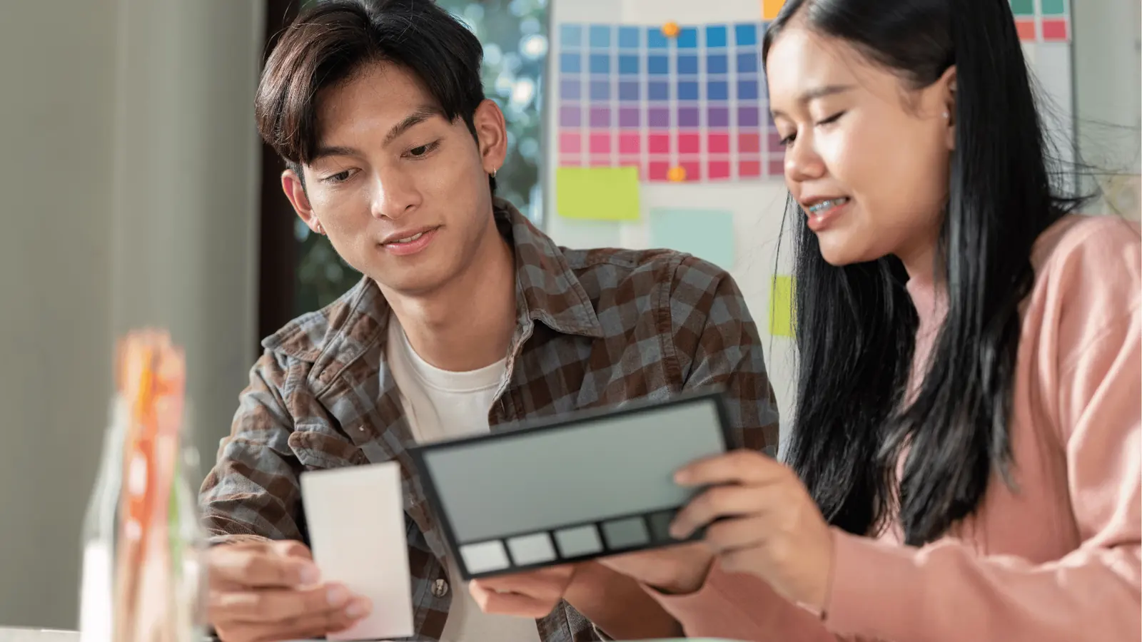 Two people comparing color swatches and a palette in a bright workspace for approval workflow