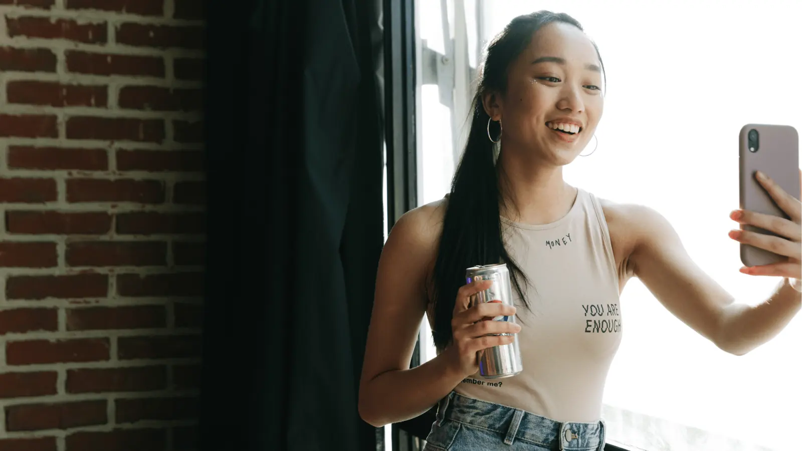Young woman smiling and taking a selfie while holding a drink for workflow