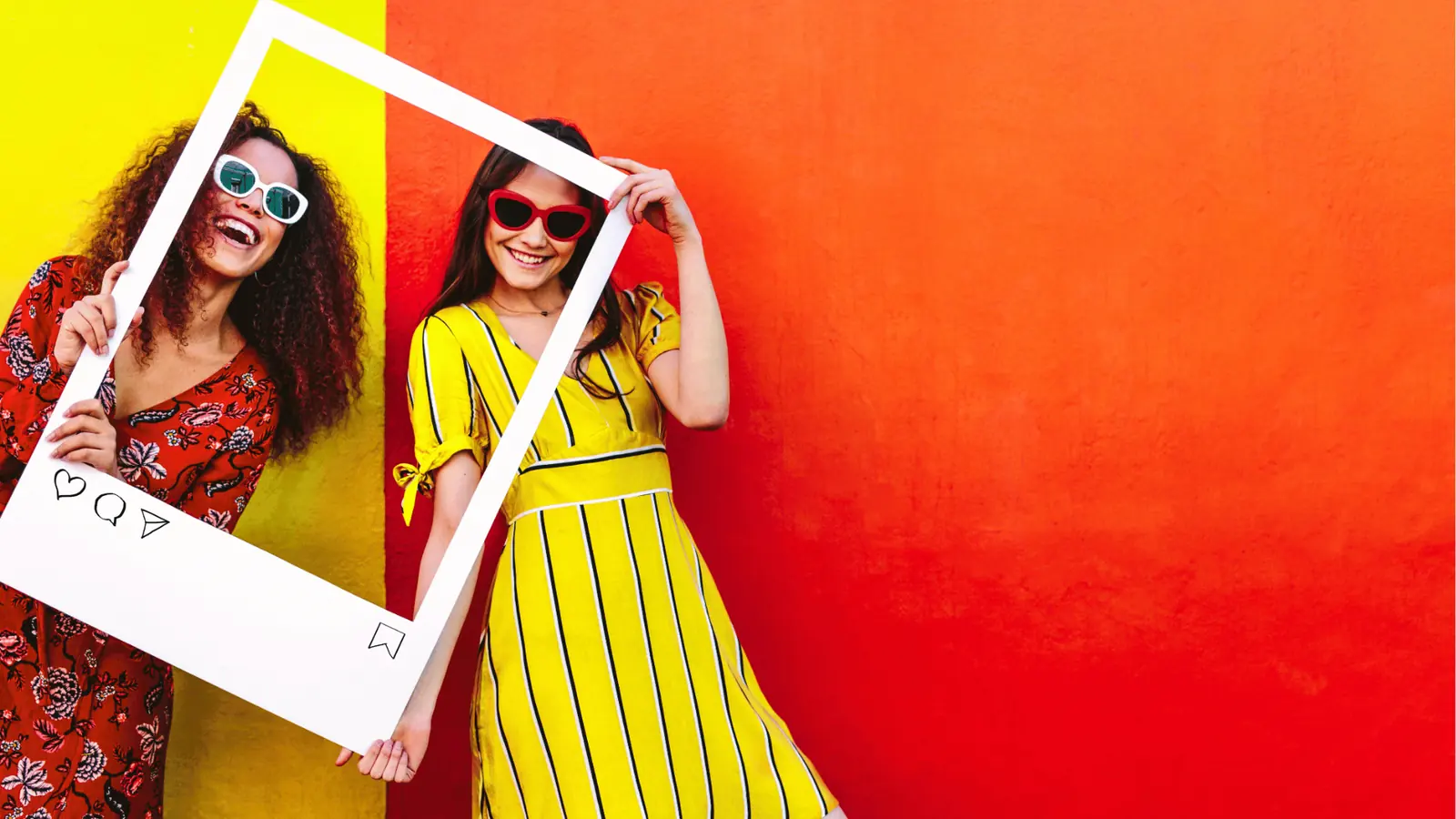 Two smiling women holding a white Instagram-style frame against colorful wall for automation