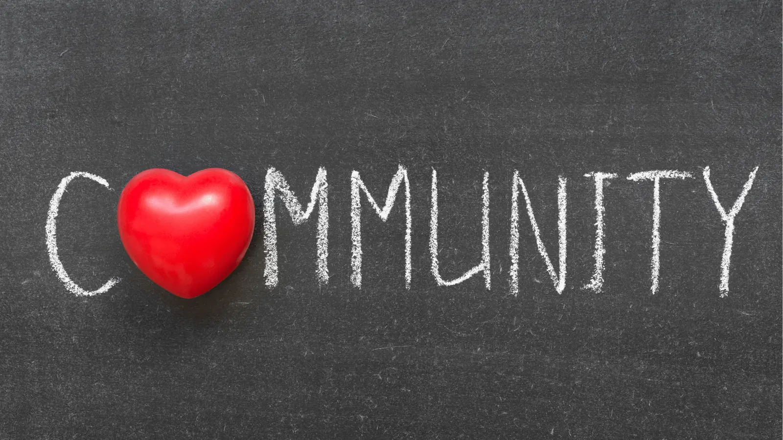 Red heart placed on a chalkboard spelling the word community in chalk for team collaboration