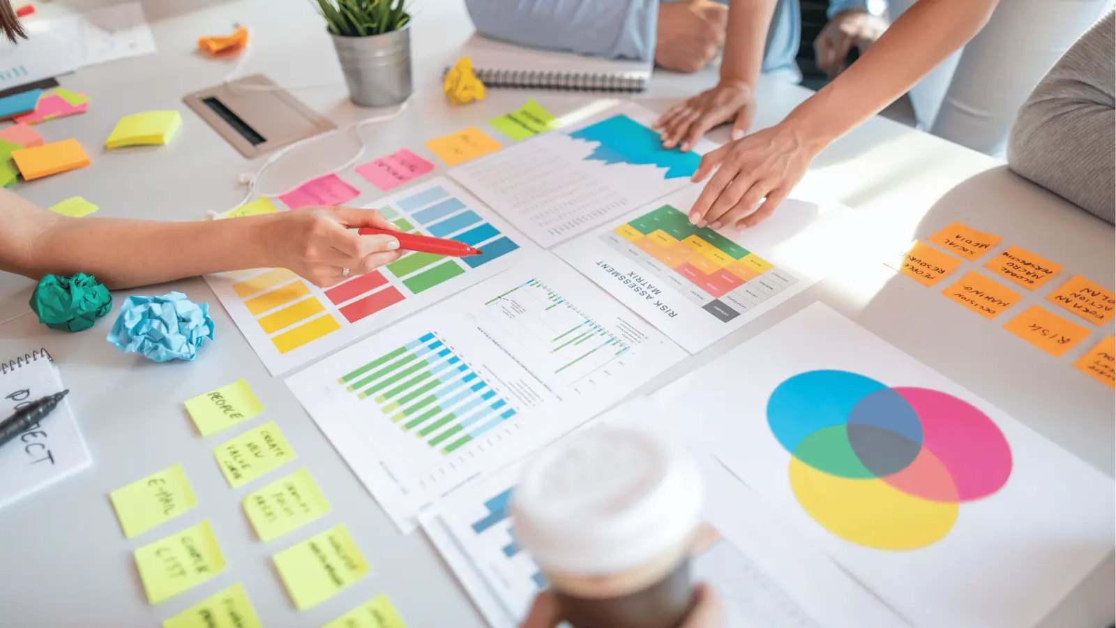 Hands pointing at colorful charts, sticky notes, and a Venn diagram on a desk