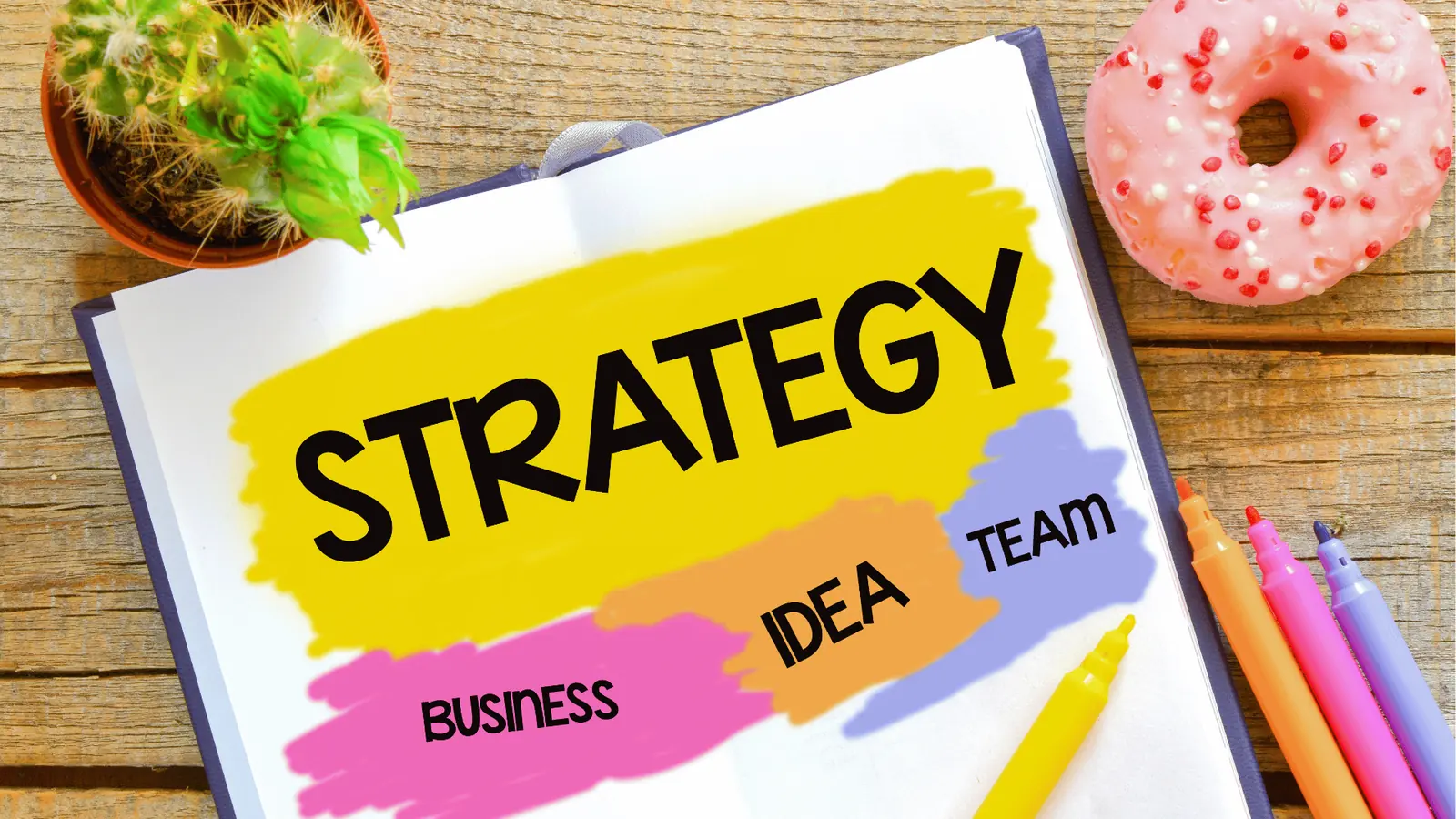 Open notebook with colorful strategy notes, markers, cactus, and pink donut for analytics