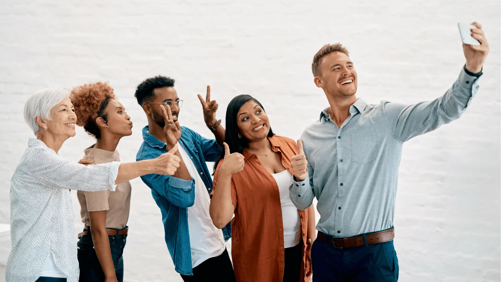 Five diverse adults smiling and posing while one man takes a selfie