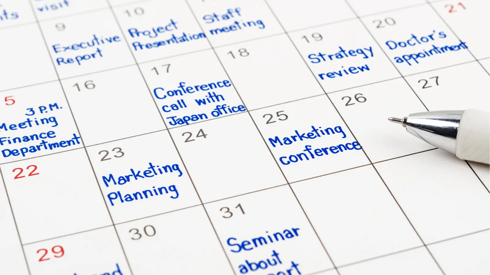 Close-up of paper calendar with blue handwritten meetings and a pen for reporting