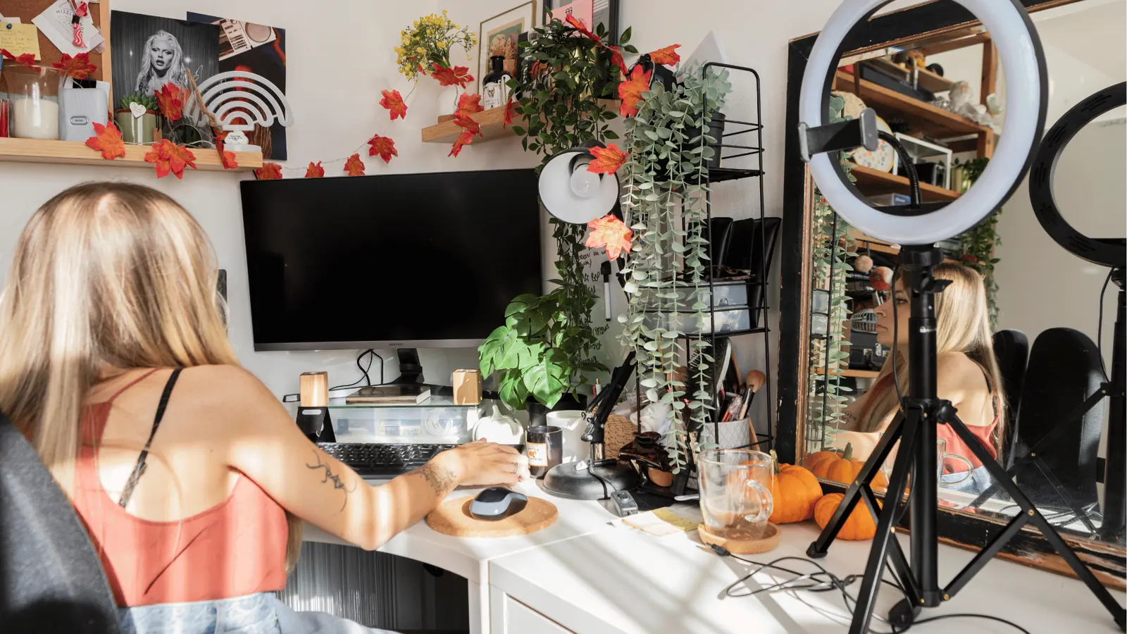 Woman at decorated home desk with ring light, monitor, plants, and pumpkins for approval workflow