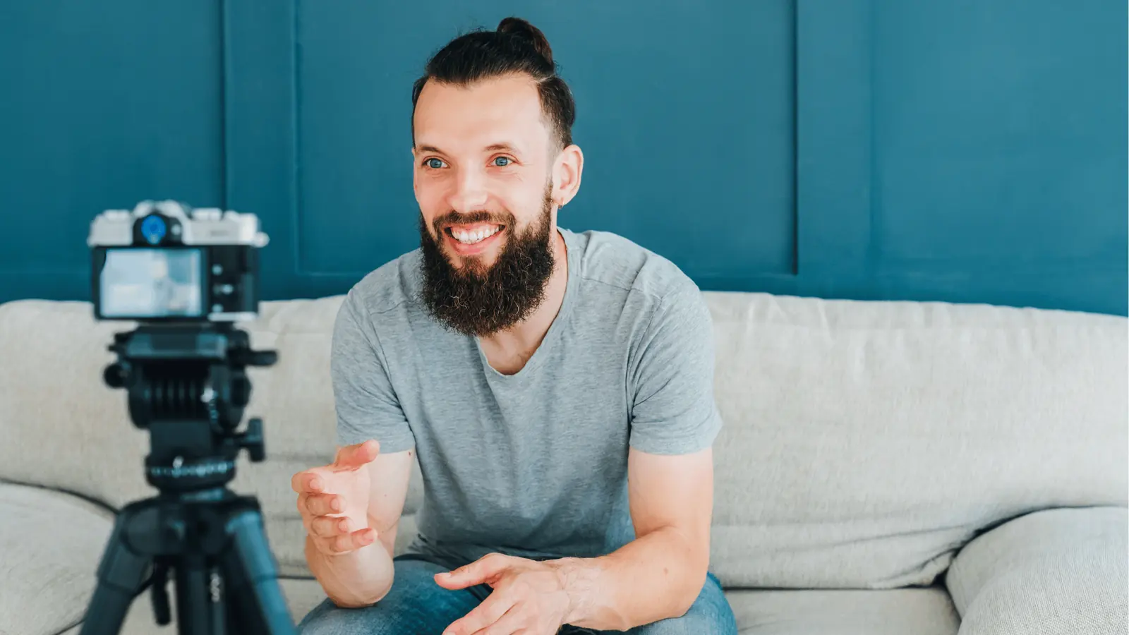 Bearded man sitting on sofa talking to camera mounted on a tripod for reporting