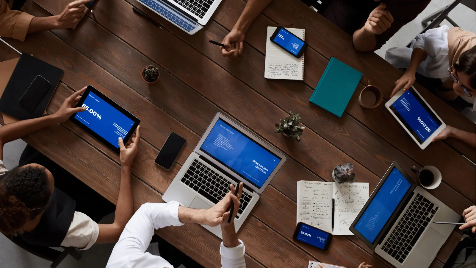 Overhead view of a team meeting with laptops, tablets, and notebooks on table for analytics