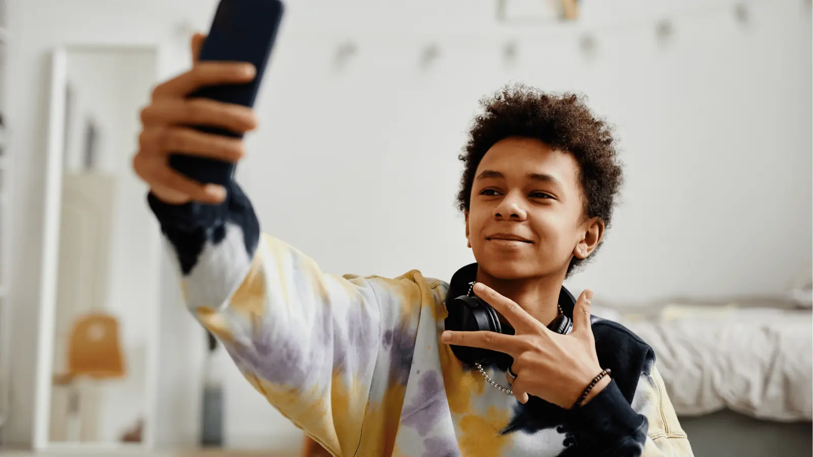 Teenager taking a selfie with headphones around his neck in bedroom for analytics