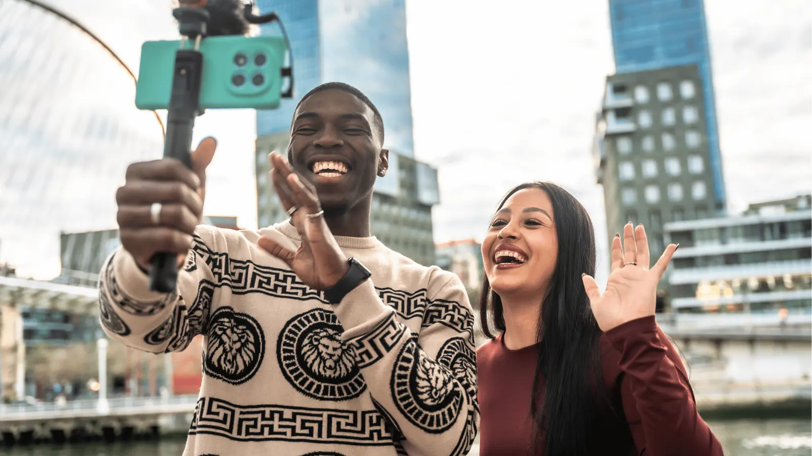Two people smiling and waving while recording a selfie video with smartphone for automation
