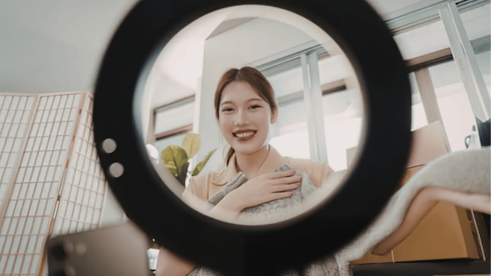 Young woman smiling at camera through ring light while holding a blanket for content calendar