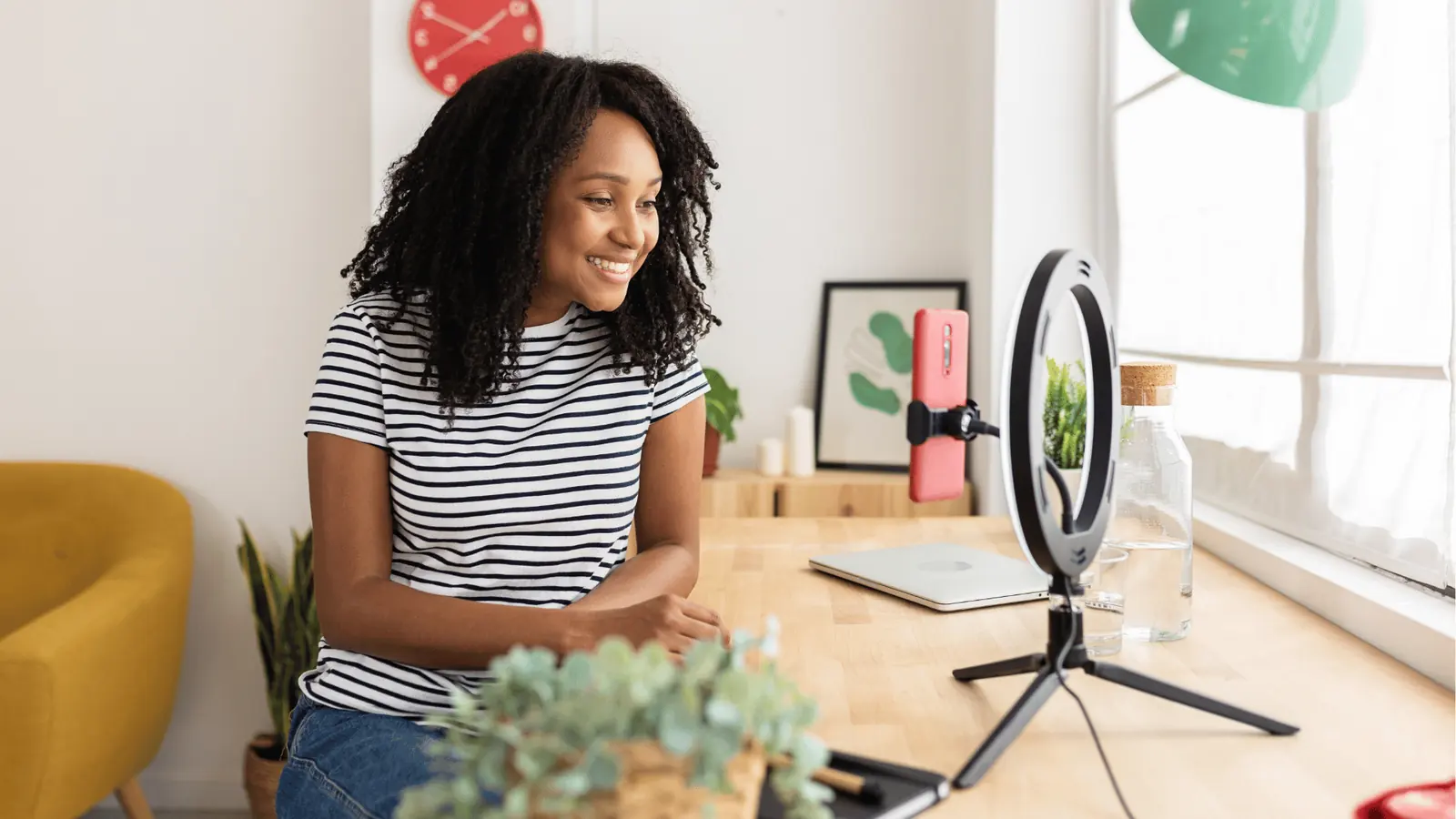 Smiling woman recording on smartphone with ring light at home desk for creative production